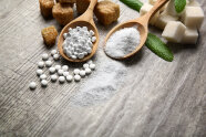 Zucker und Süßstoff-Tabletten auf Holzlöffeln, daneben Zuckerwürfel und Stevia-Blätter