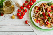 Ein Teller mit dem Mediteranen Brotsalat, daneben lauter Tomaten und Olivenöl