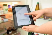 vor einem offenen Kühlschrank halten Hände ein Tablet, auf der die stocky-App zu sehen ist