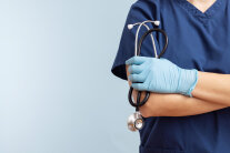 Thorso einer Person in Arztkittel, eine Hand mit blauem Gumminhandschuh hält Stethoskop