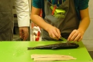 Die Hände eines Schülers setzen das Messer an, um einen Fisch zu filetieren