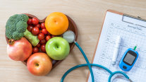 Schale mit Obst und Gemüse. Daneben liegt ein Stetoskop und ein BLutzuckermessgerät