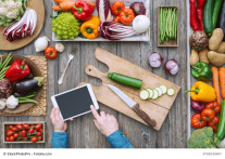 Tisch mit Gemüse, Brettchen udn MEsser udn Hände die ein Tablet bedienen